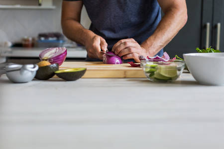 Man Slicing an Onion on a Cutting Board in a Kitchen