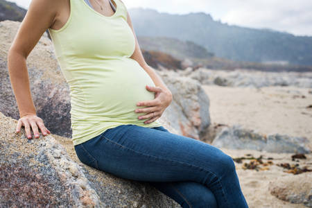 Pregnant Woman Sitting on a Rock on a Beach and Holding Her Bump