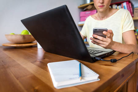 Woman Working on a Laptop from Home and Holding a Cell Phone