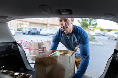 Man Loading a Shopping Bag with Groceries in a Hatchback Car