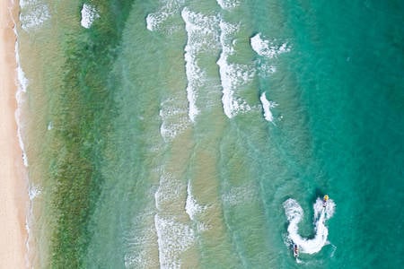 Aerial View of a Turquoise Sea Water with Jet Skis and Waves Breaking