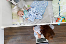 Overhead View of a Baby in a Crib and His Mom Working on a Laptop