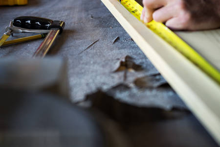 Handyman Measuring a Wooden Plank Before Cutting It with a Mitter Saw
