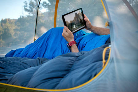Man in a Tent in a Sleeping Bag Holding a Tablet