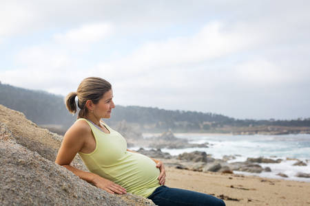 Smiling Pregnant Woman Sitting on a Rock on a Beach