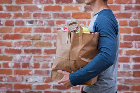 Mid-Section of a Man Carrying a Bag with Groceries on a City Street