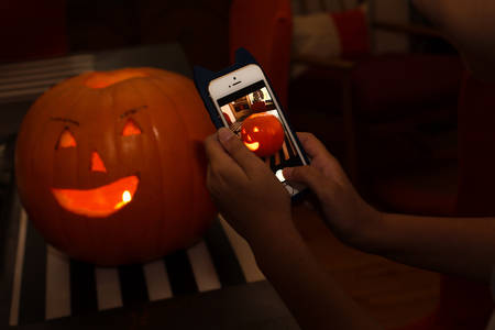 Girl Taking Picture of a Carved-Out Pumpkin with a Cell Phone