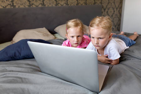 Little Twin Sisters in a Bed Watching a Movie on a Laptop