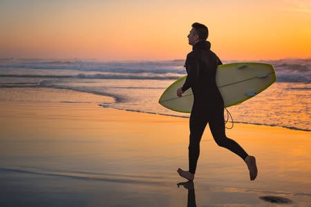 Male Surfer with a Surfboard Running on a Beach During Sunset