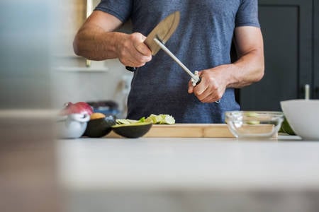 Man Standing by a Kitchen Countertop and Sharpening a Knife