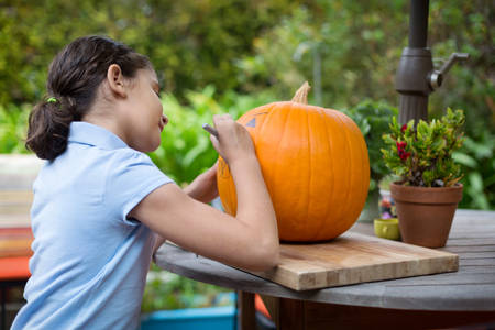 Young Girl Drawing on a Pumpkin on a Patio