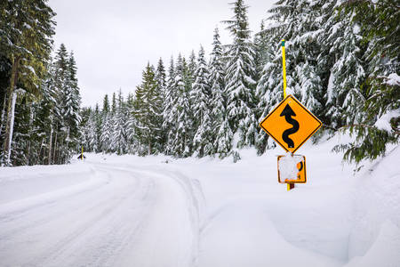 Snow-Covered Mountain Road with a Winding Road Sign