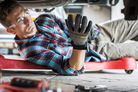Car Mechanic Putting Protective Gloves on Underneath a Truck