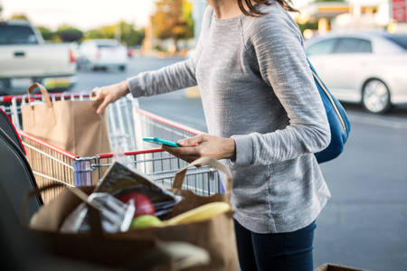Woman Unloading Paper Bags with Groceries from a Shopping Cart