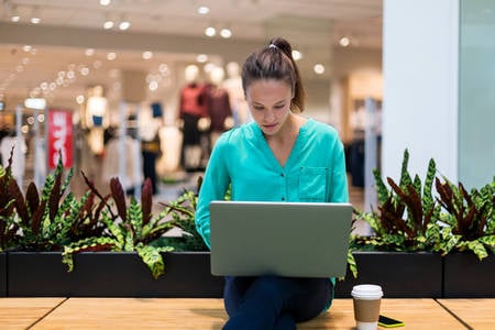 Young Woman in Casual Clothing Working on a Laptop in a Shopping Mall