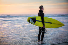 Male Surfer with a Surfboard Standing on a Beach During Sunset