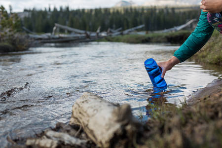 Woman Filling a Bottle with Water from a Mountain Creek