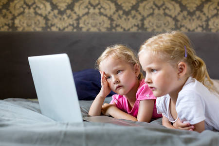 Little Twin Sisters in a Bed Watching a Movie on a Laptop