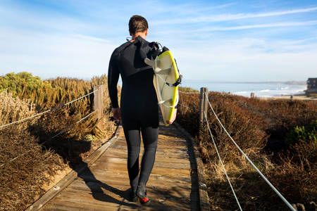 Male Surfer Carrying a Surfboard on a Wooden Path
