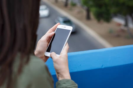 Woman Using a Cell Phone Standing on a Bridge with a Road Below