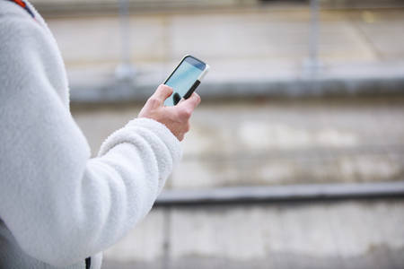 Detailed View of a Man in a White Sweater Holding a Phone in His Hand
