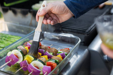   Man Braising Vegetable Skewers on a Barbecue Side Table with a Brush