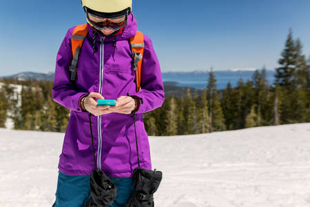 Female Snowboarder with a Cell Phone on a Top of a Ski Run