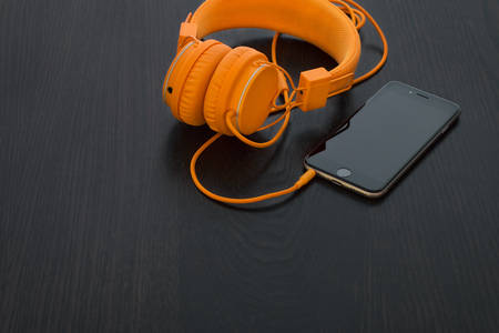 Table-Top View of a Black Cell Phone with Orange Headphones Closeby
