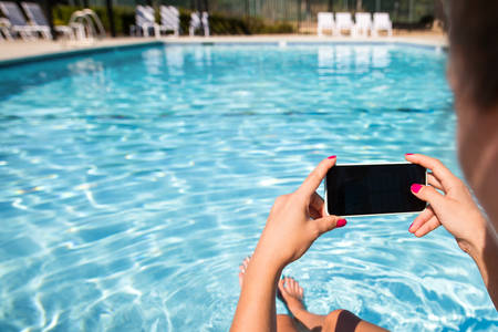 Close-Up of a Woman Siting by Pool and Taking Pictures with a Smartphone