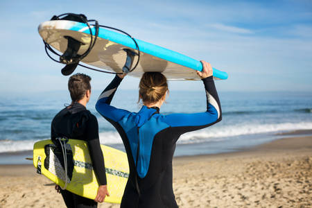 Two Surfers Walking on a Beach and Carrying Surfboards
