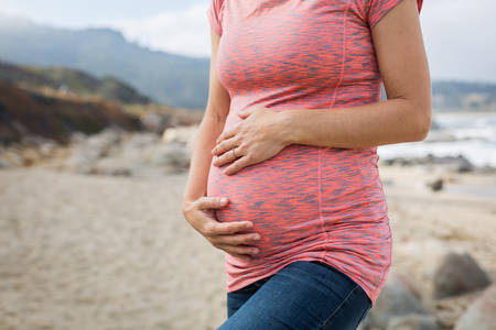 Pregnant Woman Standing on a Beach and Holding Her Bump