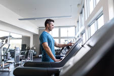 Man Selecting a Workout Setting on a Treadmill in a Gym