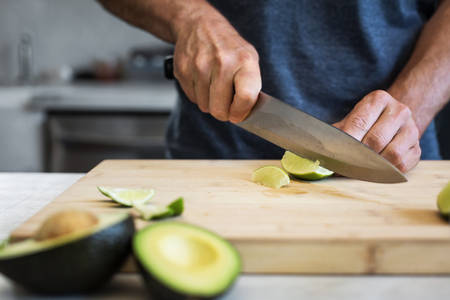  Man Cutting a Lime into Wedges on a Wooden Board in a Kitchen