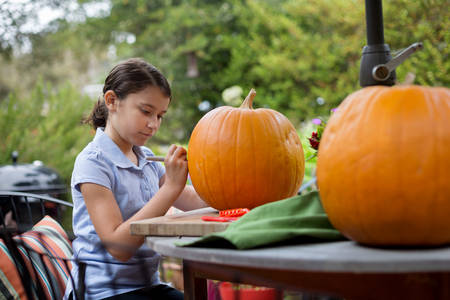 Focused Young Girl Drawing on a Pumpkin Before Carving