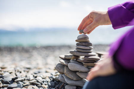 Close-Up of a Woman Stacking up Pebbles on a Beach by an Alpine Lake